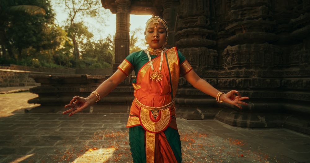 Dynamic Shot of Indian Women in Traditional Clothes Dancing Bharatanatyam in Colourful Sari Looking at the Camera.