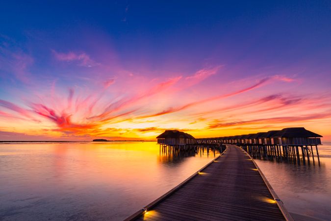 Wooden walkway towards overwater bungalows at sunset