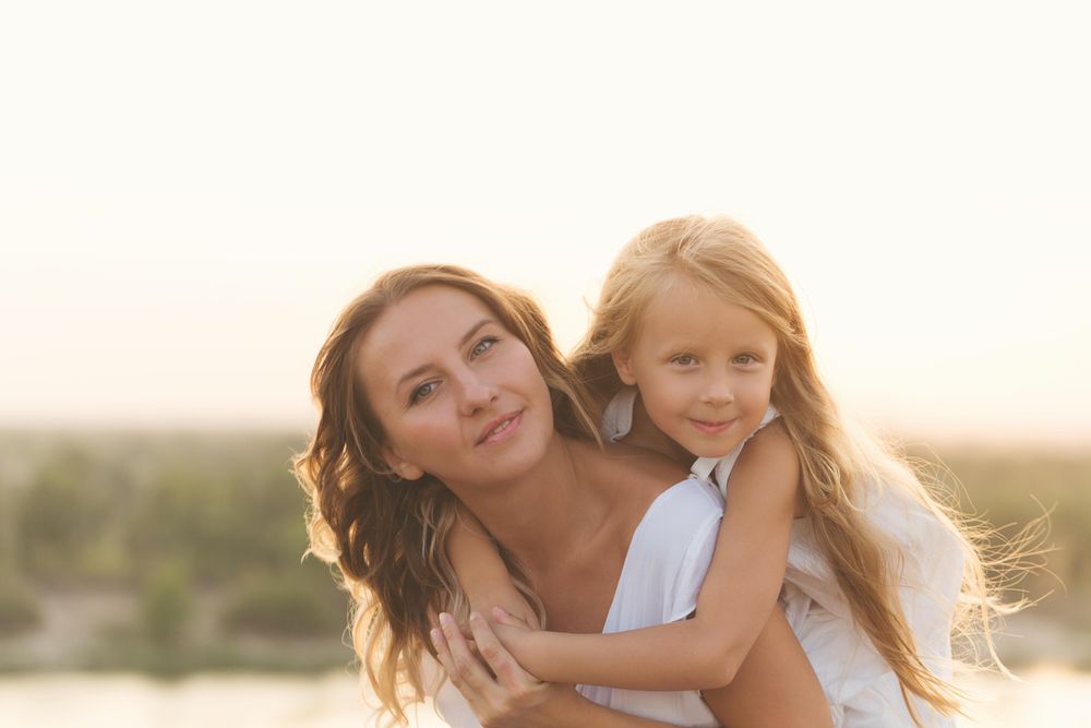 Little girl on mother’s back with lake front scenery in background