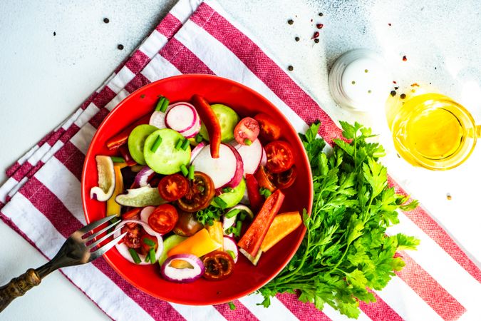 Colorful healthy raw vegetable salad served in red bowl on red striped napkin