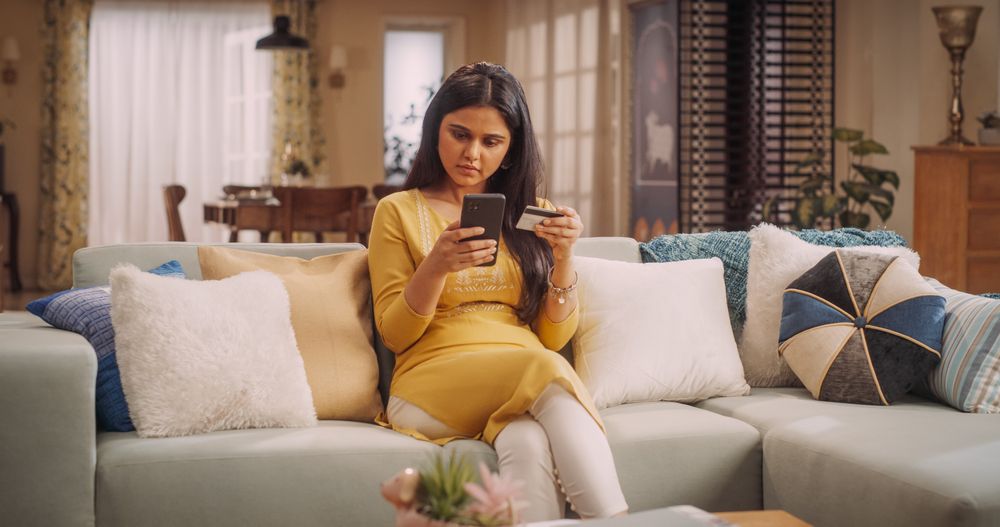 Young Indian Woman Using Smartphone and Credit Card for Online Purchase at Home