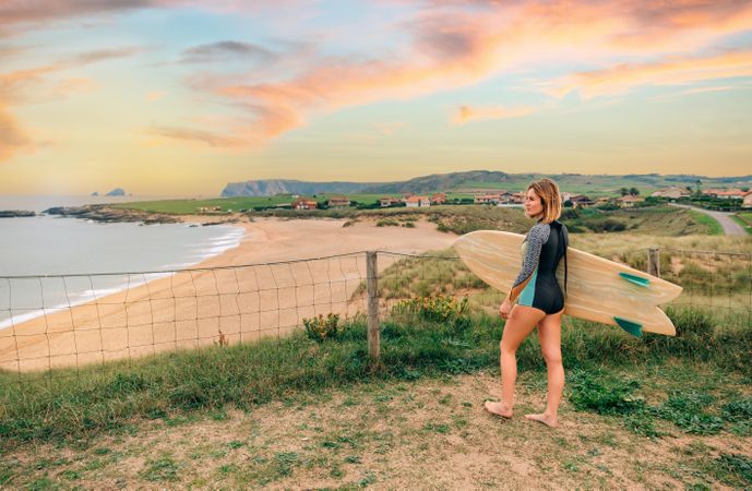 Female walking with surfboard atop of cliff with beautiful coastal view