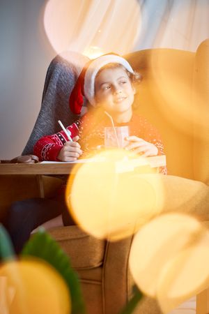 Dreamy boy in Santa hat writing on paper