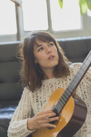 Focused female in wooly sweater looking at fretboard of guitar