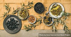 Olives in bowls with branches, on concrete with beige table linen, wide composition begRG5