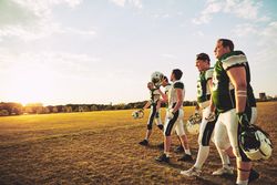 Football players walking off the pitch holding their helmets