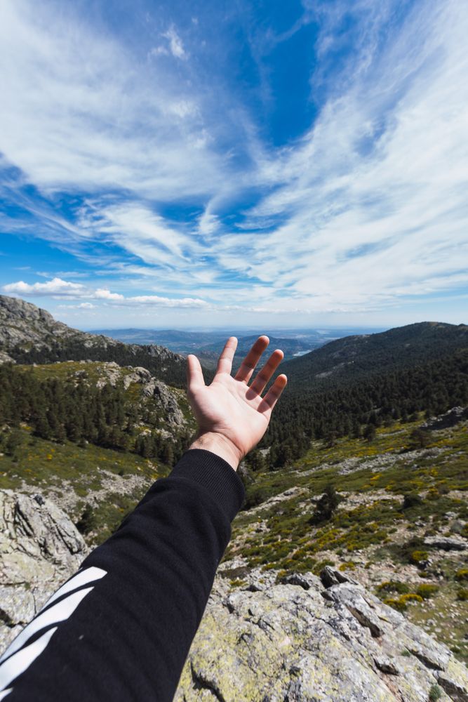 Person stretching hand to blue sky above mountain valley