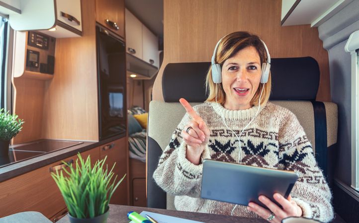Female sitting in back of camper van using digital tablet with headphones