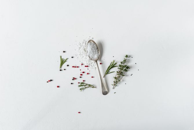Spoon of salt with herbs on light background