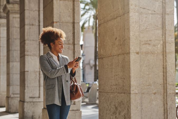 Glad Black woman using mobile phone near columns on street