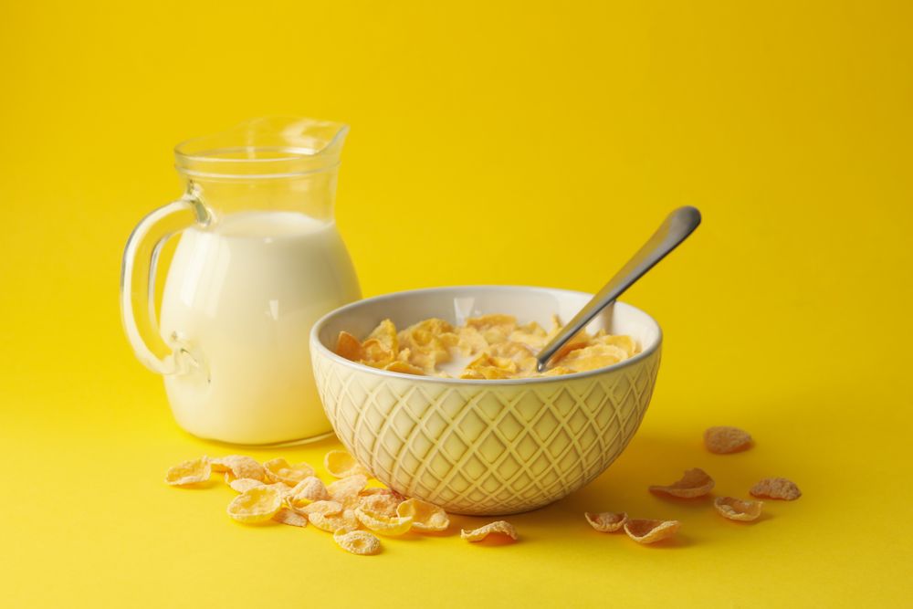 Milk and bowl of muesli on yellow background