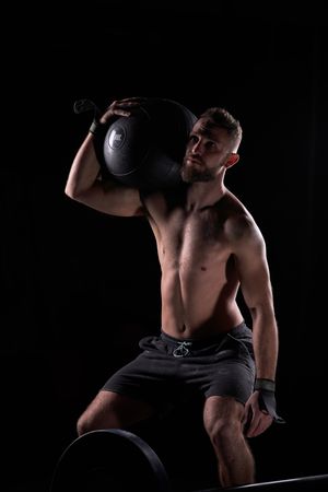 Muscular male athlete lifting fitness ball in dark gym