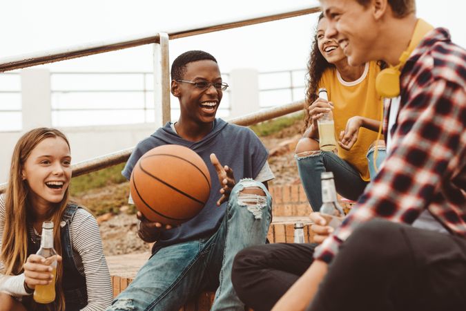 Boy holding a basketball sitting with friends on stairs having fun and laughing