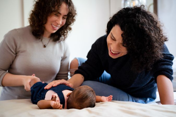 Two smiling new mothers looking down at infant on bed