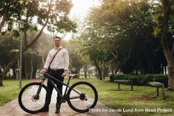 Smiling man commuting to office on a bike standing in a park with his bicycle 0LV1y4