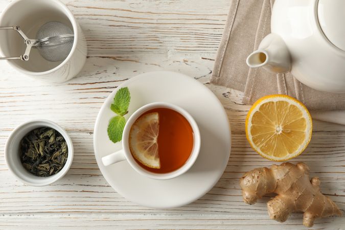 Cup of tea with lemon, mint, strainer, ginger and teapot on wooden background, top view