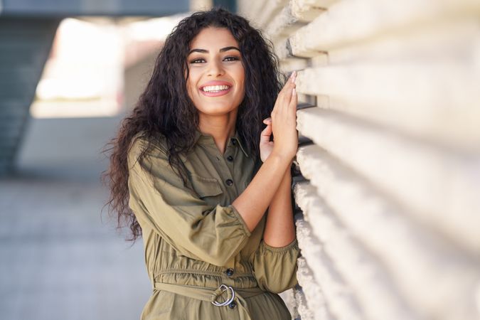 Smiling Middle Eastern woman resting on outside wall