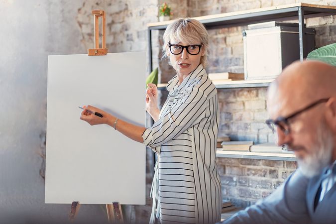 Grey haired businesswoman with marker ready to brainstorm on a blank canvas with colleagues