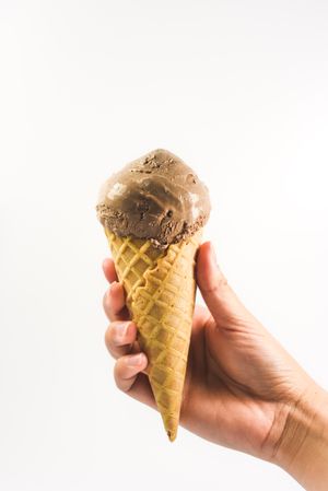 Hand holding chocolate ice cream cone on plain background
