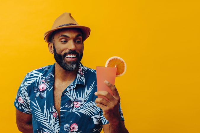 Happy male about to enjoy a cocktail while wearing colorful shirt with yellow background, copy space