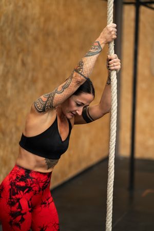 Tired fit woman climbing a rope in a gym