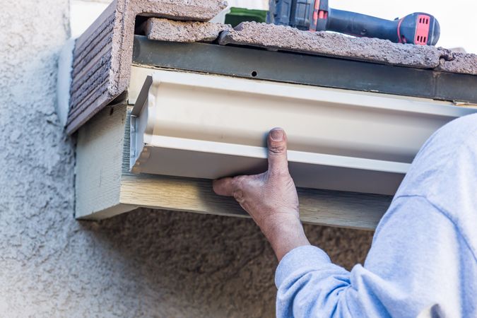 Worker Attaching Aluminum Rain Gutter to Fascia of House