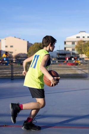 Teenage boy in yellow shirt plays basketball in public court
