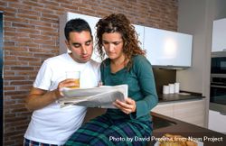 Couple in pajamas reading paper together in kitchen at breakfast time 5QEqX5