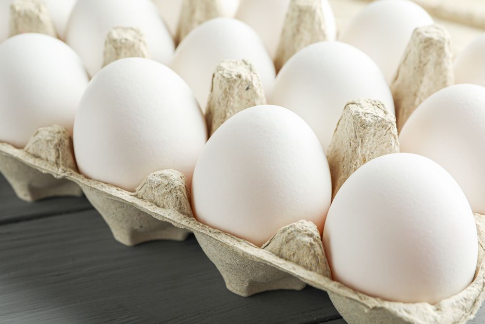chicken eggs in carton box on wooden table, space for text and closeup