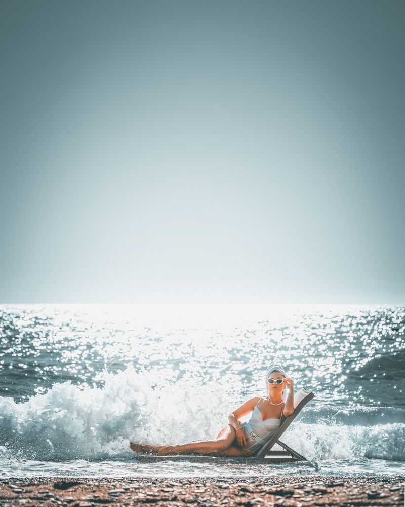 Woman in swimsuit laying on lounge chair on sea wave