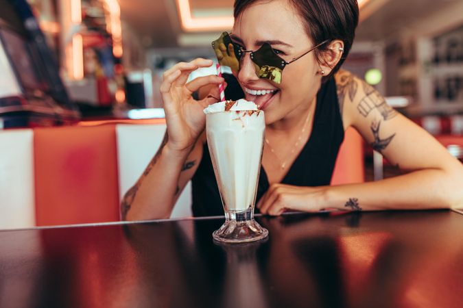 Woman wearing fancy eyeglasses sitting at a restaurant enjoying her ice cream milkshake
