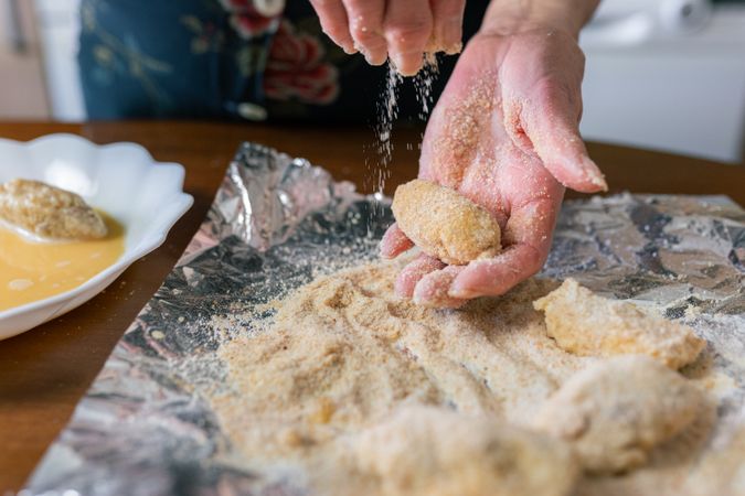 Mature woman coating croquettes with breadcrumbs at home