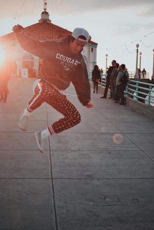 Man in hoodie jumping on street during sunset