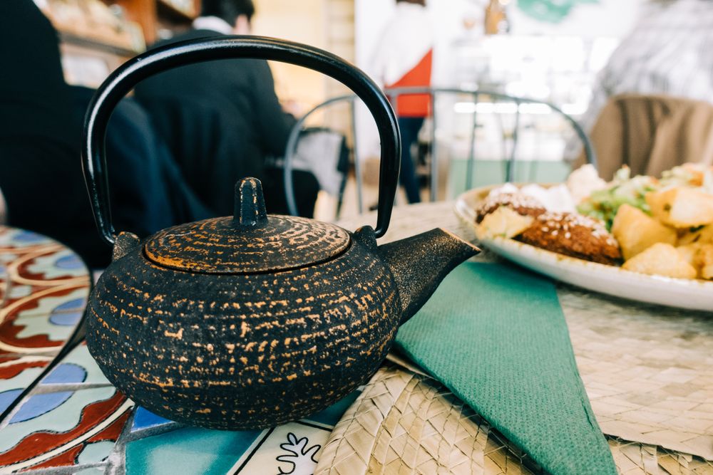 Teapot near plate with delicious food on table