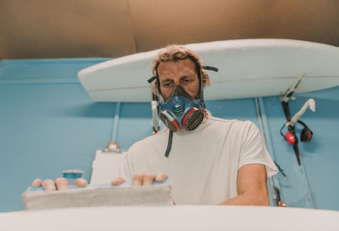 Man in respirator measuring surf board in workshop