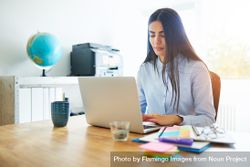 Woman in blue shirt working on her laptop in bright home office 49zQnb