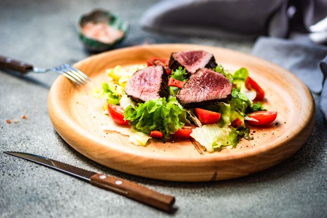 Rare steak salad with fresh lettuce on wooden plate