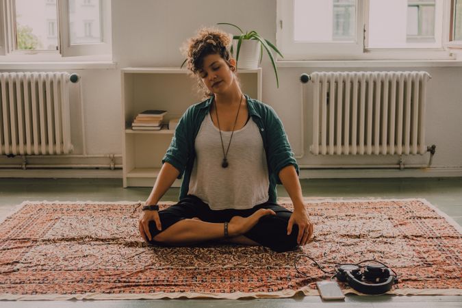 Peaceful woman meditating in lotus position on floor at home