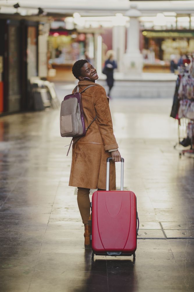 Stylish Black woman with luggage walking on street