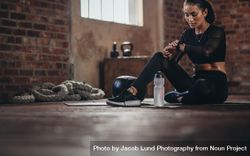 Fit young woman sitting on a floor and looking at her smartwatch at fitness studio 41X7Z5