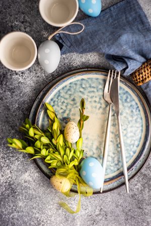Top view of Easter table setting with branch and decorative grey and blue eggs
