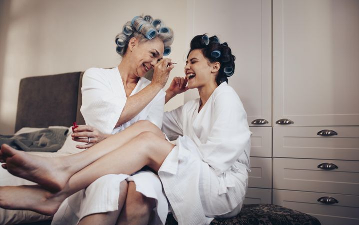 Mother and daughter in bathrobe with rollers pinned on head having fun