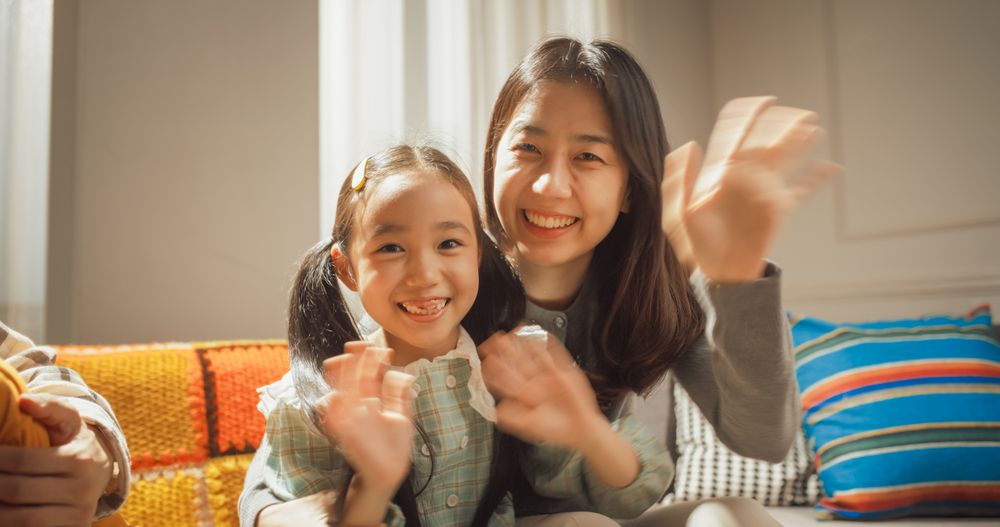 Portrait of a Happy Korean Mother and Cute Daughter at Home, Smiling and Waving at the Camera.