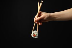 Female hand with chopsticks hold sushi roll on dark background. Japanese food