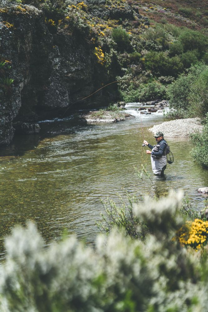 Confident man fishing with rod while standing in river stream