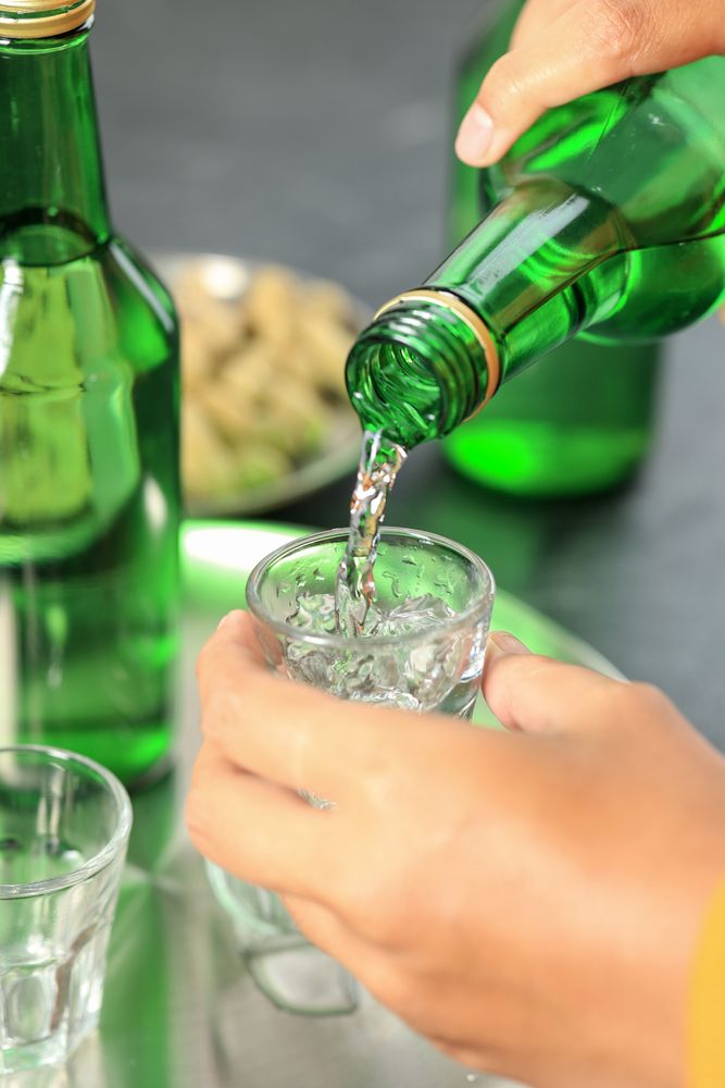 Person pouring soju into glass cup