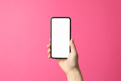 Female hand holds phone on pink background. Empty screen