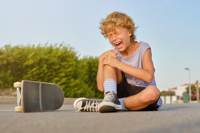Boy crying after falling off skateboard in city