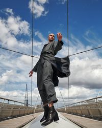 Stylish young man in gray coat and pants looking around on bridge