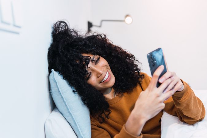 Happy Black female with cellphone in bed